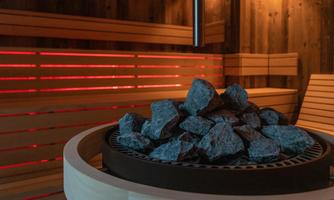 A modern sauna area with a stone kettle. The walls are made of wood and softly lit.