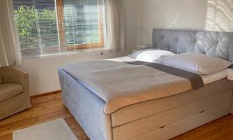A bright bedroom with a cozy double bed and a comfortable armchair. Large windows let in plenty of daylight.