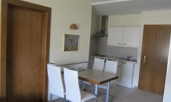 A cozy kitchenette with a dining table and white chairs. The walls are light, and there is wooden paneling on the doors.