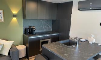 A modern kitchen unit with dark cabinets and an elegant countertop. In the foreground, a cozy seating area with a gray sofa.