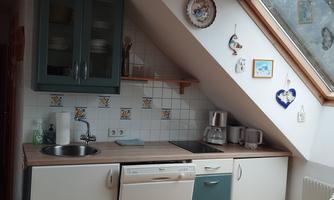 A modern kitchen with slanted walls and wooden flooring. It includes a dishwasher, a sink, and decorative wall panels.