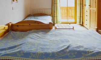 A cozy bedroom with two single beds and bright curtains. The room has a large window front that lets in plenty of daylight.