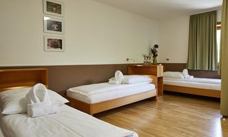 A simple room with three single beds and light wood furniture. The walls are painted in soft colors, and there is a green curtain layer.