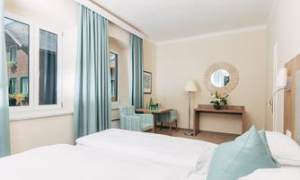 A bright room with two beds, a desk, and a cozy seating area. The walls are painted in soft colors, and large windows let in plenty of daylight.