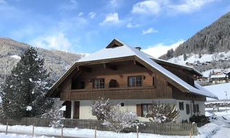 A charming wooden house in the snow, surrounded by a picturesque mountain landscape. The sky is clear, and the atmosphere feels peaceful.