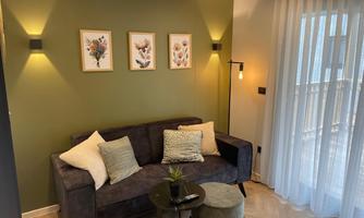 A cozy living room with a gray sofa and decorative pillows. Three pictures hang on the wall and the windows are adorned with light curtains.
