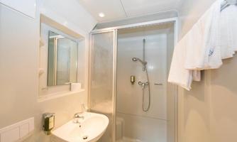 A modern bathroom with a shower and a sink. The walls are light, and there are large mirrors as well as towels.