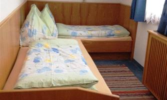 A simple bedroom with two beds and colorful blankets. The room has a carpet and curtains that let light in.