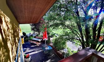 A cozy terrace with garden furniture and colorful flowers. In the background, green meadows and trees can be seen.