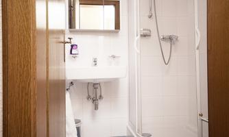 A modern bathroom with a shower, a sink, and a mirror. The walls are tiled white and the floor is blue.