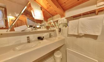A modern bathroom with two sinks and large mirrors. The wooden ceiling gives the room a cozy atmosphere.