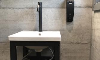 A modern sink on a stylish stand in a room with a gray wall. There is a soap dispenser on the wall.