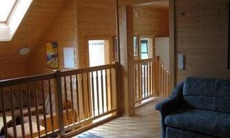 A bright wooden interior with an open staircase and a cozy sofa. The walls are made of wood and there is a window with daylight.