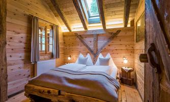 A cozy bedroom with wooden walls and a large bed. The room has large windows that let in natural light.