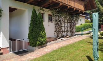 A beautiful house with a well-maintained garden. Visible are a green hedge and a gate that leads to a small path.