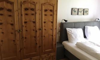 A cozy bedroom with a large bed and a wooden wardrobe. Three pictures are hanging on the wall.