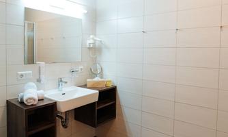A modern bathroom with a white sink and a large mirror. The walls are brightly tiled, and there are towels and some toiletries.