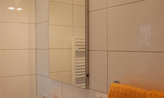 A modern bathroom with white tiles and a large mirror. On the vanity, there are orange towels and toiletries.
