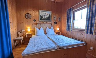A cozy bedroom with two single beds and wooden walls. The room has a windowsill with a view and is simply but invitingly furnished.