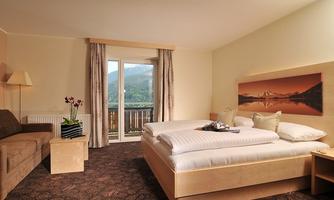 A modern hotel room with a large bed and a cozy sofa. Through the window, you can see the mountains and nature.