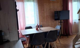 A cozy interior with wooden walls. In the center is a dining table with chairs and a television in the corner.
