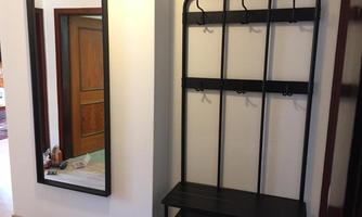 A modern hallway with a large wall mirror and a black coat stand. The floor is bright and the background features a wooden door.
