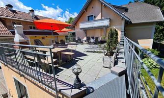 A modern house with a terrace and a large sun umbrella. The surroundings are bright and inviting, ideal for sociable hours outdoors.