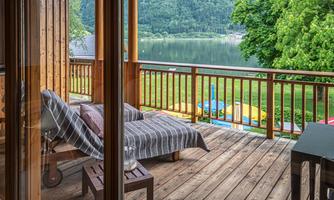 A cozy terrace with a view of a lake and lush green trees. Two loungers are ready to enjoy the view.