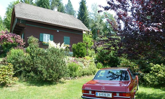 A beautiful wooden house with a colorful garden and many plants. In front of the house stands a red car.