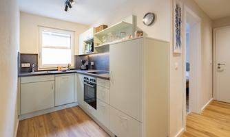 A modern kitchen with bright cabinets and wooden flooring. The windows provide lots of daylight.