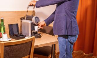 A man is preparing coffee with a coffee machine at a table. In the background, you can see a bottle of water and a cup.