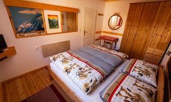 A cozy bedroom with two beds and warm wooden details. The walls are decorated with pictures and a mirror, creating an inviting atmosphere.