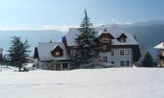 A picturesque house in a snowy landscape. Surrounded by fir trees and with a clear blue sky in the background.