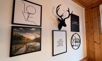 A wall with various frames and artworks. Below are a landscape photograph, decorative texts, and antlers as wall decoration.