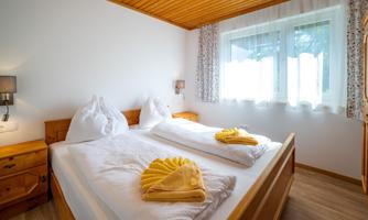 A cozy bedroom with two single beds and wooden details. Fresh towels and a bright room create an inviting atmosphere.