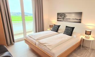 A bright bedroom with a double bed and two nightstands. Large windows provide a view of the landscape.