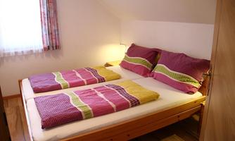 A cozy bedroom with two single beds. The bed linen is designed in colorful stripes, and a window lets in natural light.