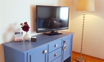 A cozy room with a blue TV table and a television. Next to the table is a floor lamp and a vase with flowers.