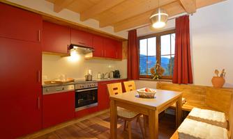 A modern kitchen with red cabinets and a wooden cupboard. The table is decorated with fresh fruit and offers space for four people.