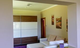 A modern living room with white sofas and a purple carpet. There is a large window front and a bright, welcoming atmosphere.