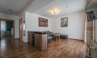A modern living room with wooden flooring and a dining area. The walls are painted light and decorated with artworks.