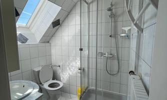 A bathroom with a shower and toilet. The walls are tiled, and there is a window that lets in natural light.