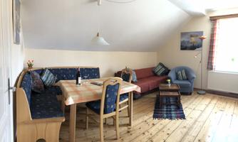 A cozy living space with a wooden floor and a dining table. The seating area is inviting and decorated with cushions.