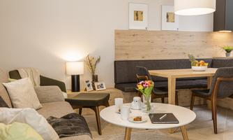 A cozy living room with modern furniture and a dining area. Fresh flowers and some drinks are on the table.