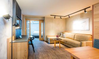A modern living and bedroom with a cozy sofa and a wooden table. Large windows provide plenty of light and a bright atmosphere.