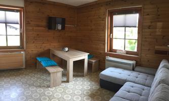 A cozy room with wooden walls and a modern sofa. There is a table with benches and two windows that let in plenty of light.