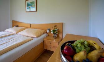 A cozy bedroom with a double bed and fresh flowers on the nightstand. In the foreground, there is a bowl of colorful fruit.