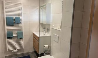 A modern bathroom with white tiles and wood shavings. There is a sink, a shower, and towels in shades of blue.