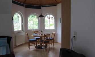 A cozy dining area in a bright room with round windows. A round table with chairs is in the center, next to it is a small television.