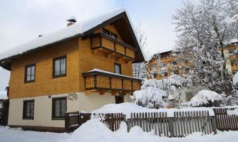 A cozy wooden house in the snow, surrounded by a picturesque winter landscape. The sky is cloudy and the snow covers the ground.